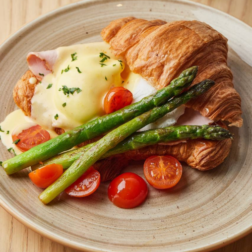 Poached eggs with Hollandaise sauce on croissant with asparagus